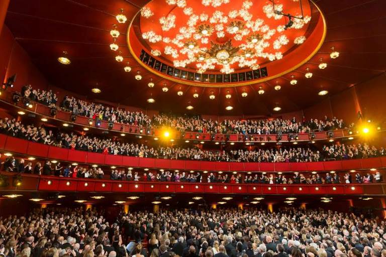 草莓视频免费版app Opera House with elaborate chandelier on the ceiling and a full house applauding an honoree in the Presidential Box.