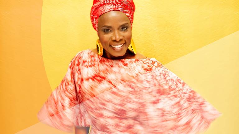 Angelique Kidjo smiling with red wrap and yellow background