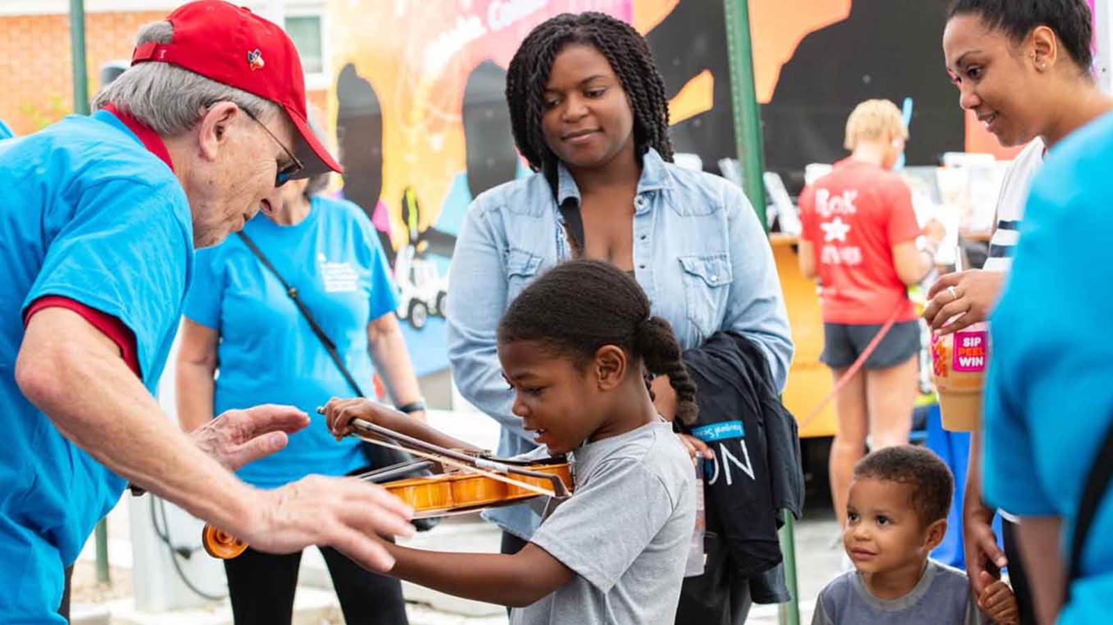 A child learns the violin from an NSO volunteer. 