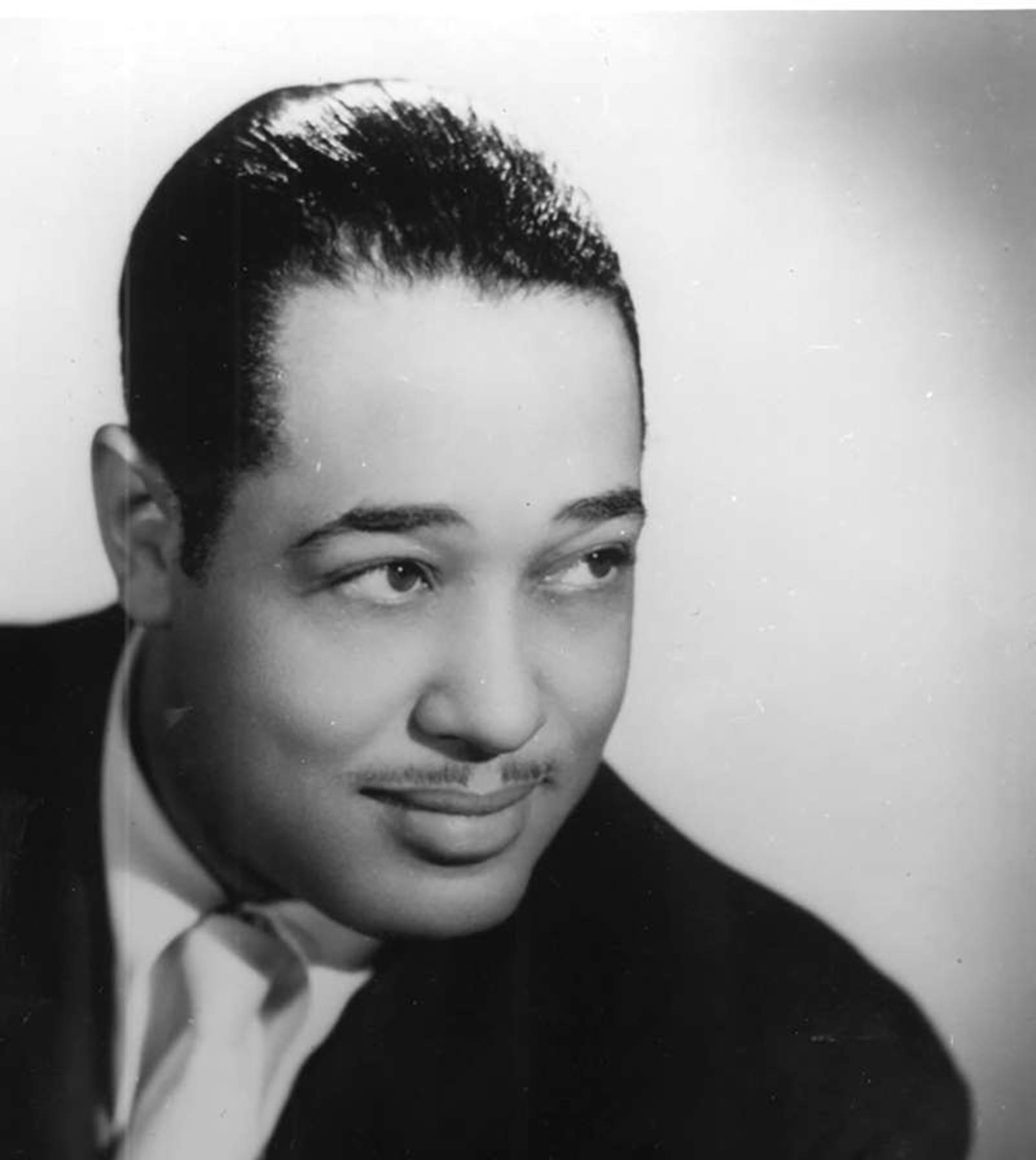A young Duke Ellington gazes off camera with a smile in black and white photo